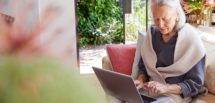 Seniorin sitzt mit dem Laptop auf dem Sofa