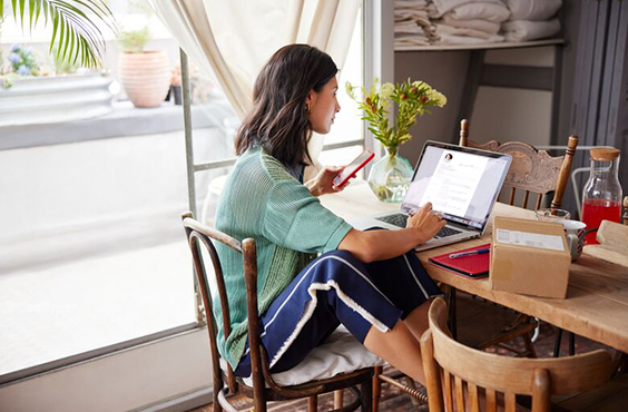 Frau arbeitet am Laptop, Smartphone in der Hand