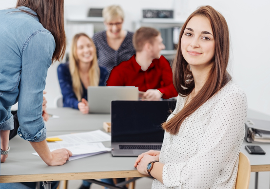 Lehre Applikationsentwicklung – Coding - Junde Frau vor Laptop, Team im Hintergrund