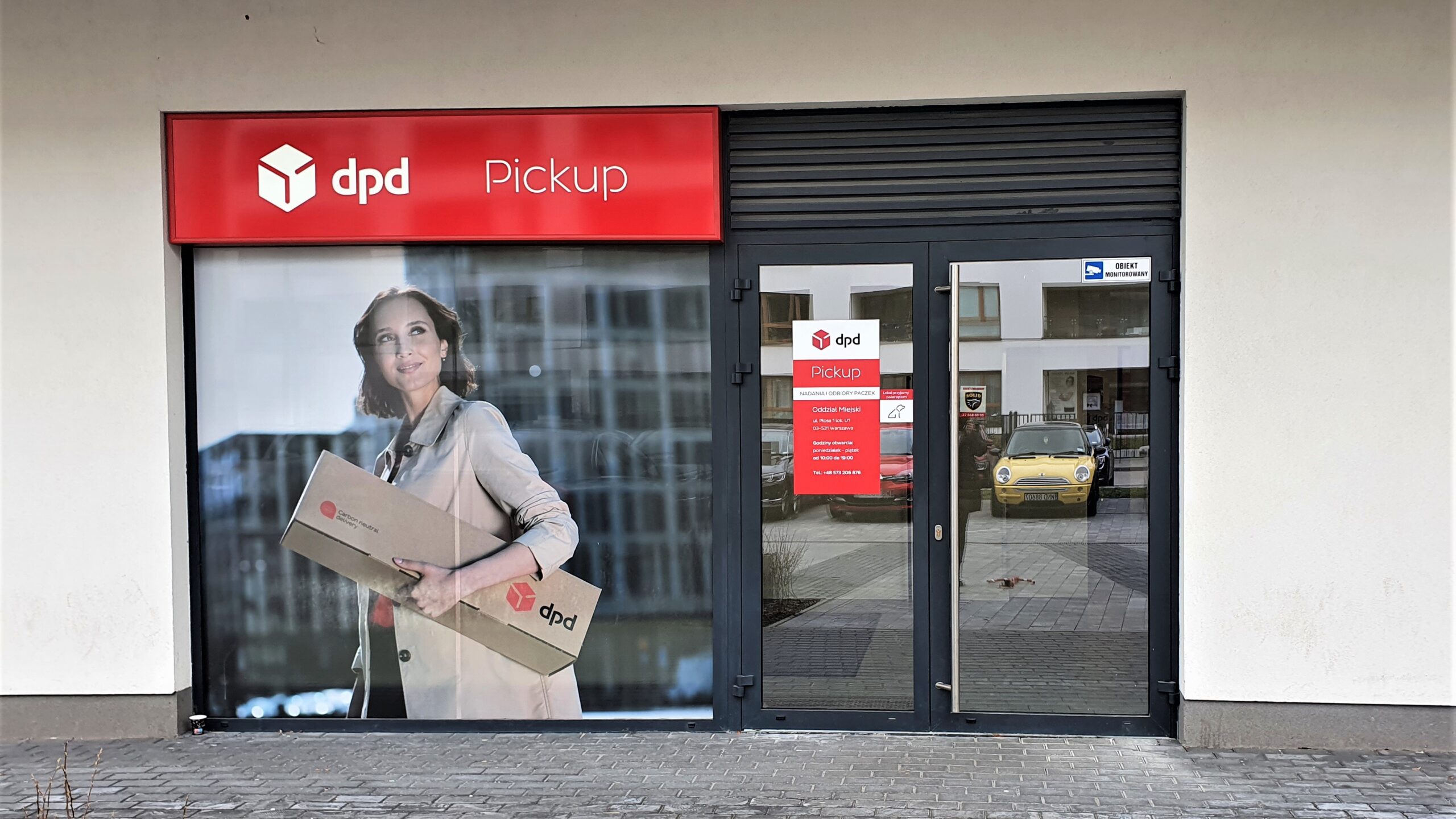 Punkt DPD Pickup. Nad wejściem szyld z logo i napisem Pickup. Na witrynie grafika z paczką.
