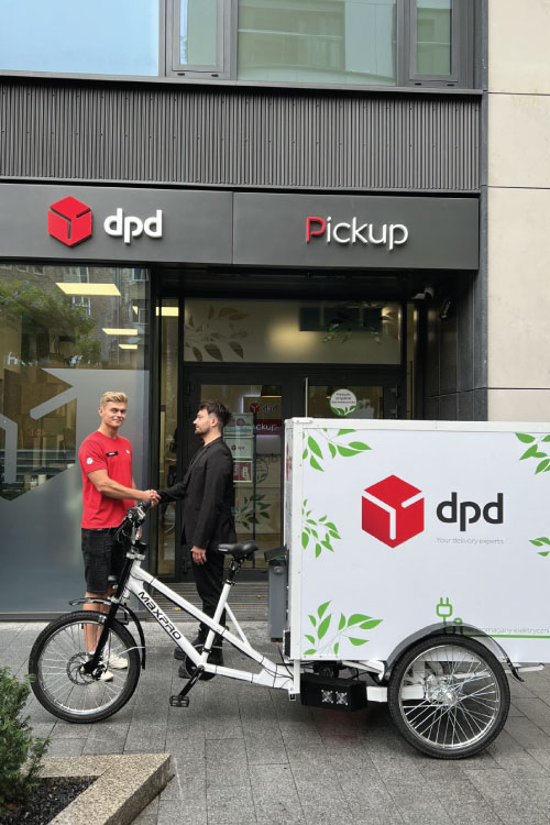 Kurier DPD wita klienta przy rowerze cargo przed punktem DPD Pickup.