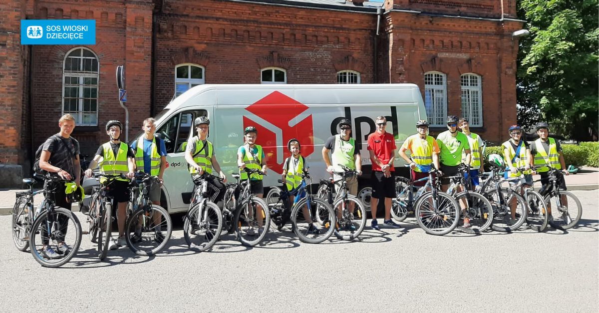 Grupa rowerzystów w kamizelkach DPD przed furgonetką DPD.