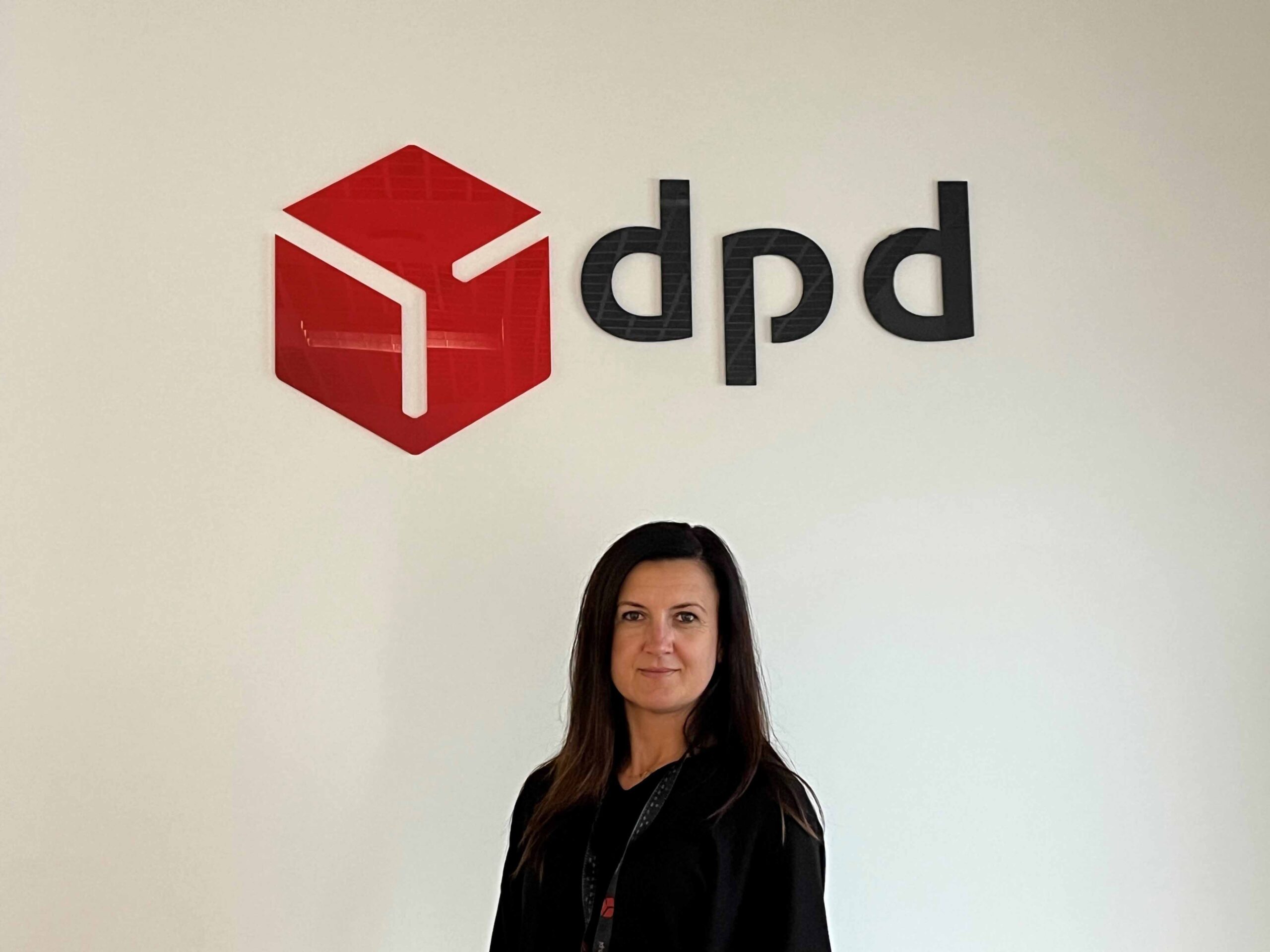 Kobieta na tle ściany z logo DPD Polska. Profesjonalny portret pracownika firmy.