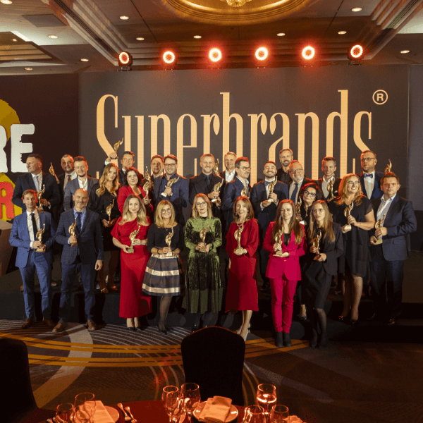 Grupa osób z nagrodami Superbrands na tle logotypu konkursu.