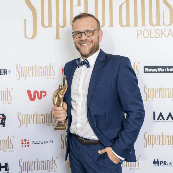 Mężczyzna z nagrodą Superbrands Polska na tle logotypów.