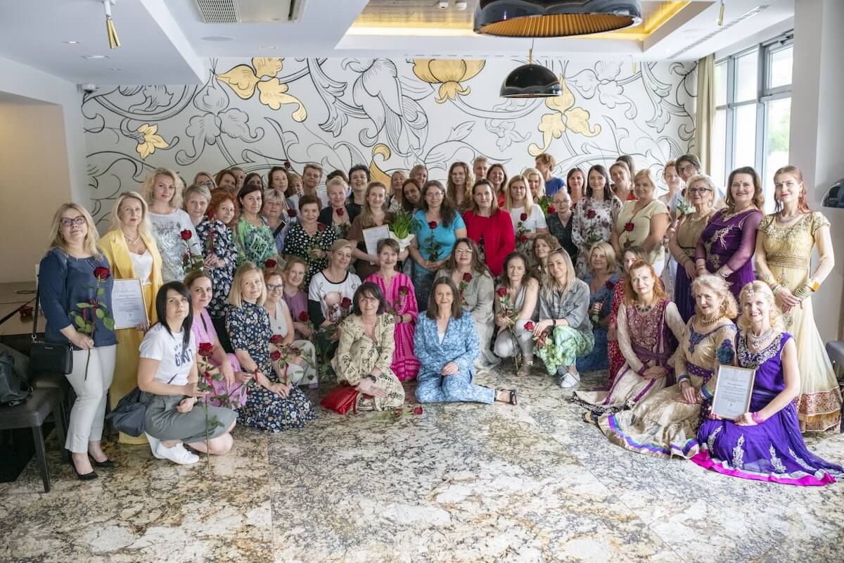 Grupowe zdjęcie kobiet z różami i dyplomami w eleganckim wnętrzu.
