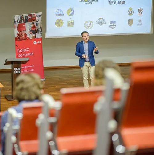 Prelegent prowadzący wykład podczas finału I Beskidzkiej Olimpiady Logistyczno-Transportowej na Uniwersytecie Bielsko-Bialskim, na tle baneru DPD Polska i logotypów firm partnerskich.
