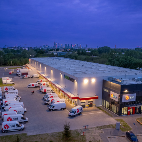 Centrum logistyczne DPD z flotą pojazdów dostawczych na tle panoramy miasta.