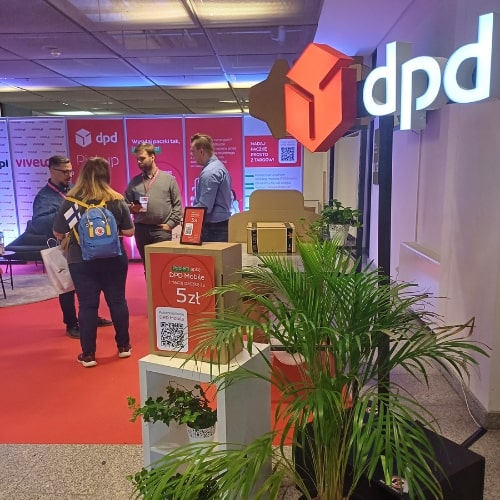 Stoisko DPD na targach Vivelo 2024, gdzie kilka osób rozmawia z przedstawicielami firmy. Na pierwszym planie widać rośliny oraz ekspozycję promującą usługi DPD, w tym DPD Mobile.