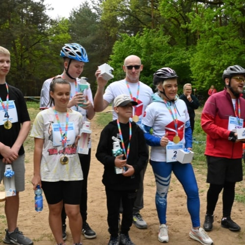 Uczestnicy triathlonu młodzieżowego DPD po ceremonii wręczenia nagród, trzymający medale i upominki. Wszyscy są uśmiechnięci i stoją razem, pozując do zdjęcia.
