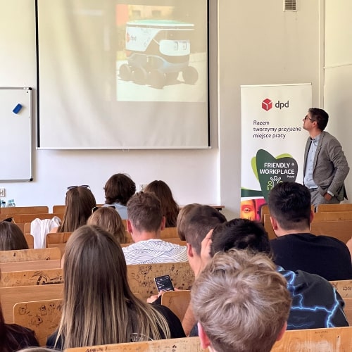 Prezentacja DPD: robot dostawczy na ekranie, słuchacze i prelegent.