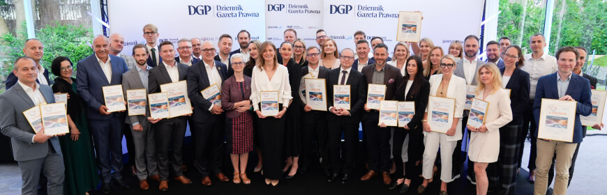 Duża grupa osób pozująca razem do zdjęcia, trzymająca certyfikaty i uśmiechająca się. Stoją na tle z logo DGP (Dziennik Gazeta Prawna). Wygląda to na ceremonię wręczenia nagród.