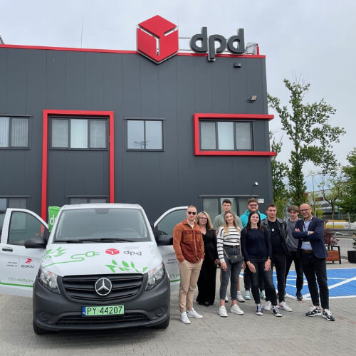 Grupa osób przed budynkiem DPD i samochodem dostawczym z logo firmy.