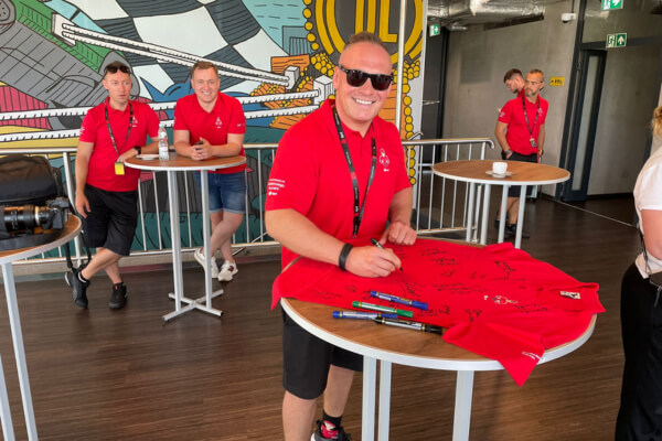 Mężczyzna w czerwonej koszulce DPD składa autograf na koszulce.