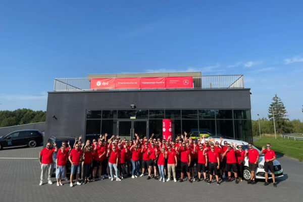 Grupa pracowników DPD przed budynkiem firmy, w czerwonych koszulkach.