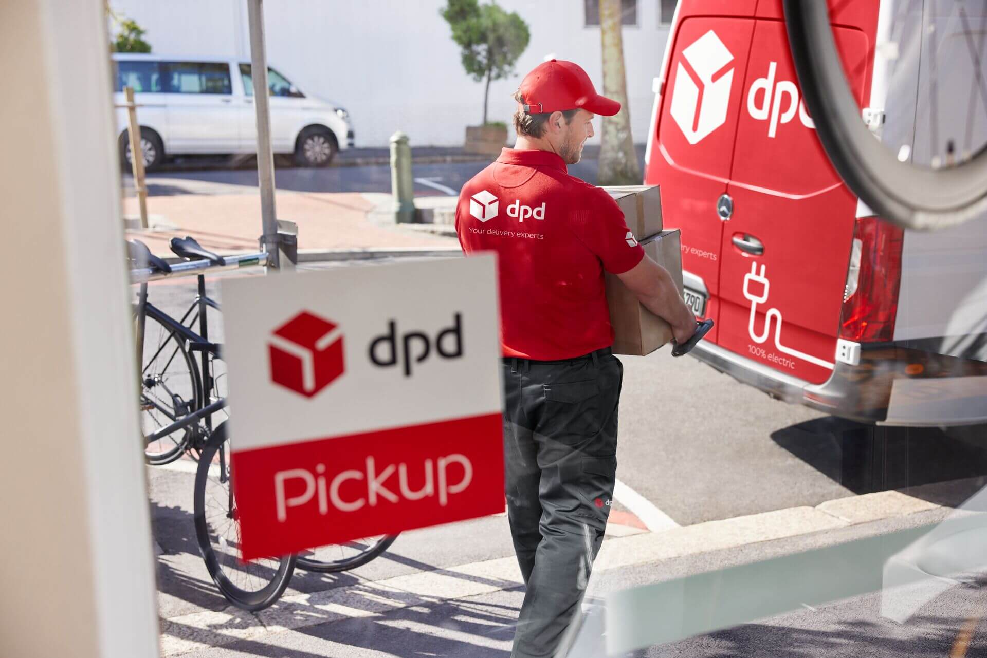 Kurier DPD z paczkami przy elektrycznym samochodzie dostawczym i punkcie Pickup.