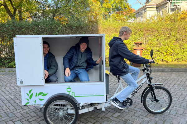 Uczniowie siedzą w przestrzeni ładunkowej roweru cargo DPD, testując funkcjonalność tego ekologicznego środka transportu podczas festiwalu.