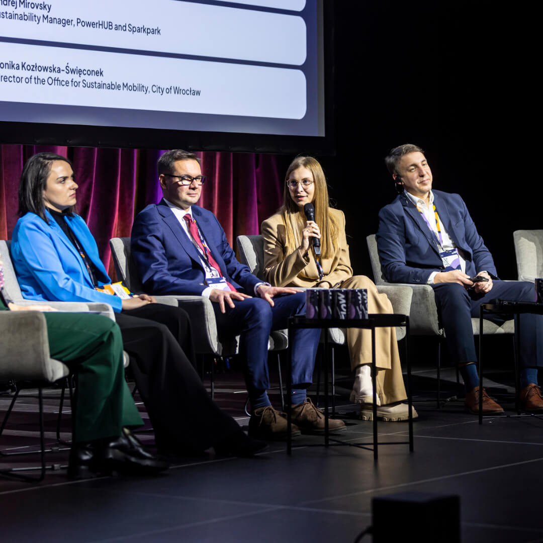 Projekt bez nazwy (76) Uczestnicy panelu dyskusyjnego siedzą na scenie podczas Urban Mobility Flow Summit 2024 w Gdańsku. Monika Grąbczewska z DPD Polska zabiera głos, omawiając zrównoważoną logistykę miejską. W tle widoczne są informacje o uczestnikach na ekranie.