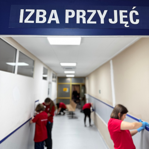 Projekt bez nazwy (95) Wolontariusze malują ściany w szpitalnym korytarzu, tablica "Izba Przyjęć" u góry.
