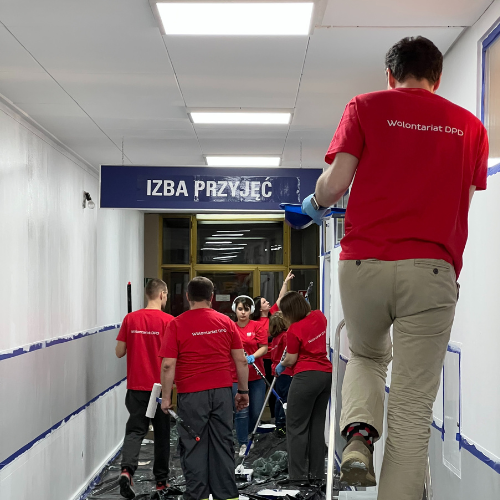 Projekt bez nazwy (96) Wolontariat DPD maluje ściany w Izbie Przyjęć. Grupa osób w czerwonych koszulkach.