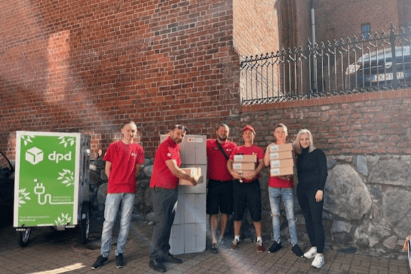 Grupa wolontariuszy DPD Polska w czerwonych koszulkach pozuje obok automatu paczkowego i roweru cargo. Na zdjęciu widoczne są paczki, które zostały przygotowane jako upominki dla dzieci z przedszkola Krucza Chatka.