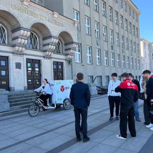 Kobieta na ekologicznym rowerze cargo DPD Polska przed budynkiem Uniwersytetu Morskiego, promująca zrównoważone dostawy.