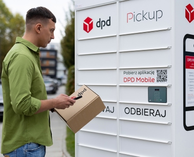 Mężczyzna z paczką i telefonem w dłoniach stoi przed białym automatem paczkowym z logo DPD Pickup