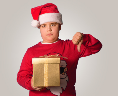A kid with an unhappy face gives thumbs down while holding a present