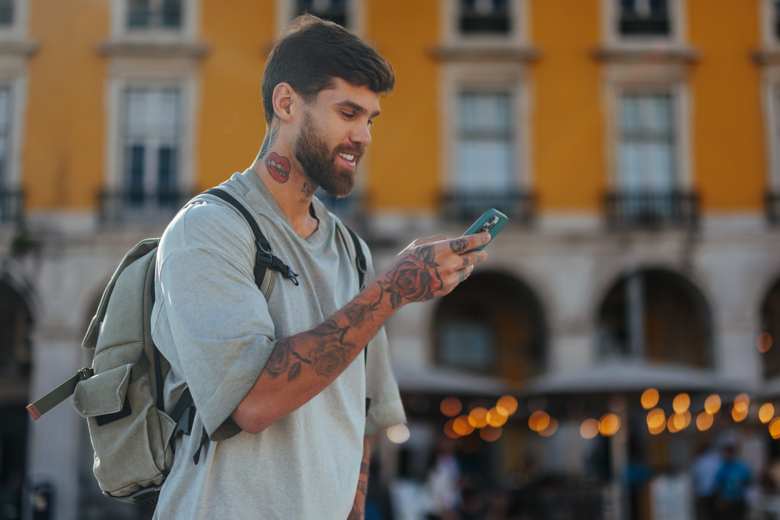 Uśmiechnięty mężczyzna w tatuażach z pleackiem patrzy na telefon
