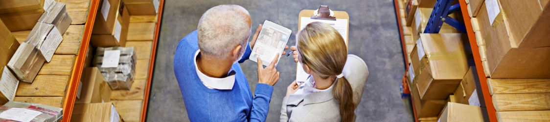 Dwoje pracowników przeglądających dokumenty w magazynie pełnym kartonów