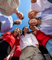 Eine Gruppe von acht jungen Erwachsenen steht im Kreis und schaut nach unten zur Kamera.
