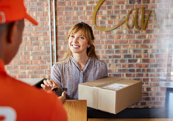 Lächelnde Kundin nimmt ein Paket von einem DPD-Zusteller entgegen und bestätigt die Zustellung digit