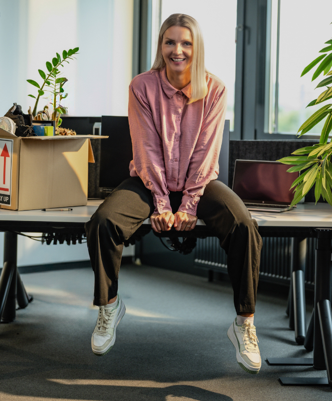 Frau sitzt auf ihrem Schreibtisch am neuen Arbeitsplatz